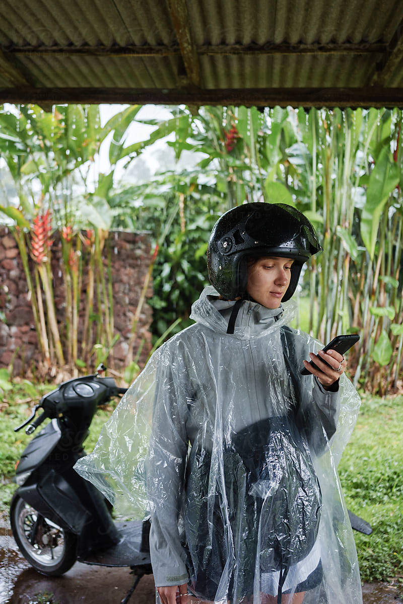 Person in Rain Gear Checking Phone Under Shelter