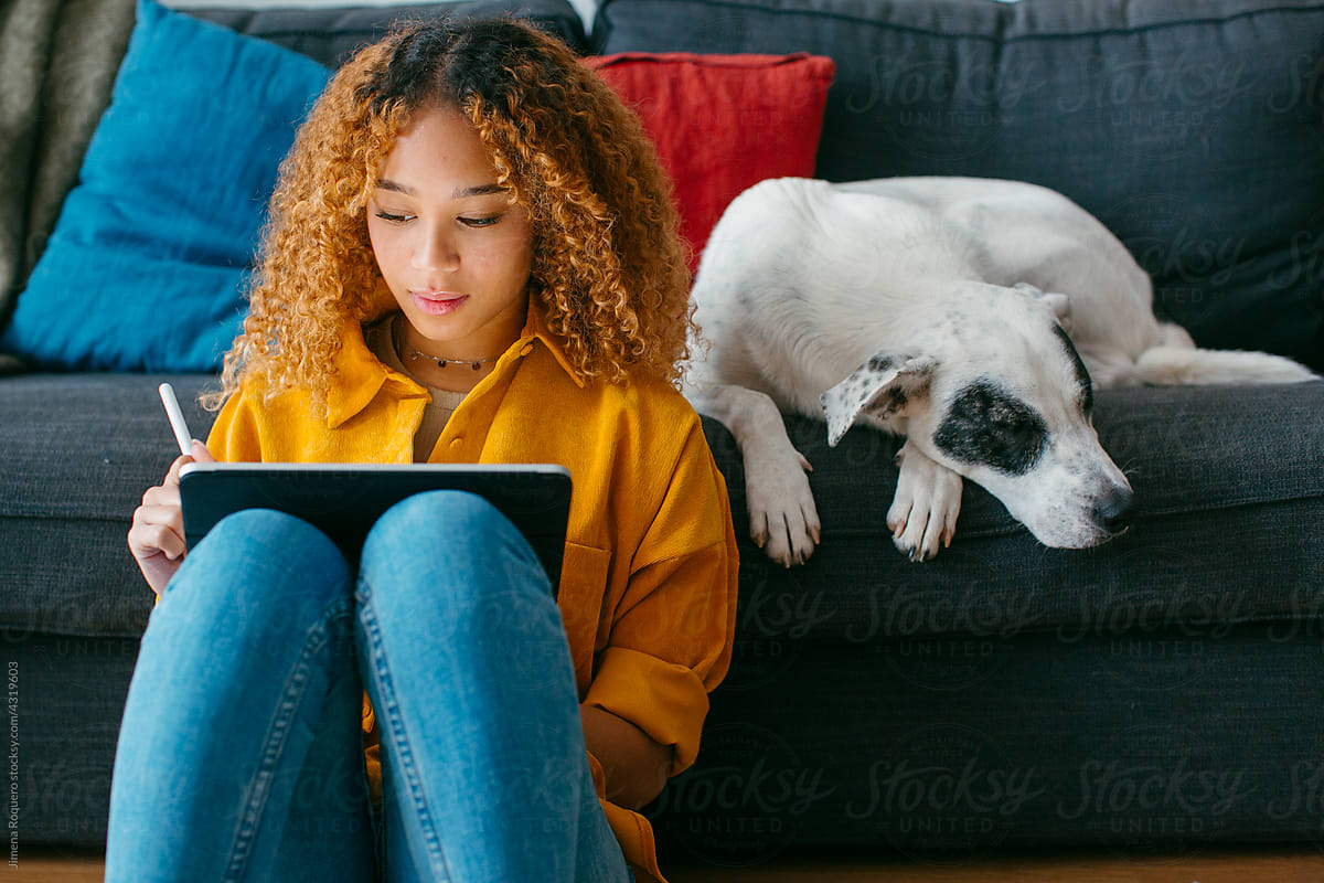 Teenager at home living room using tablet petting dog