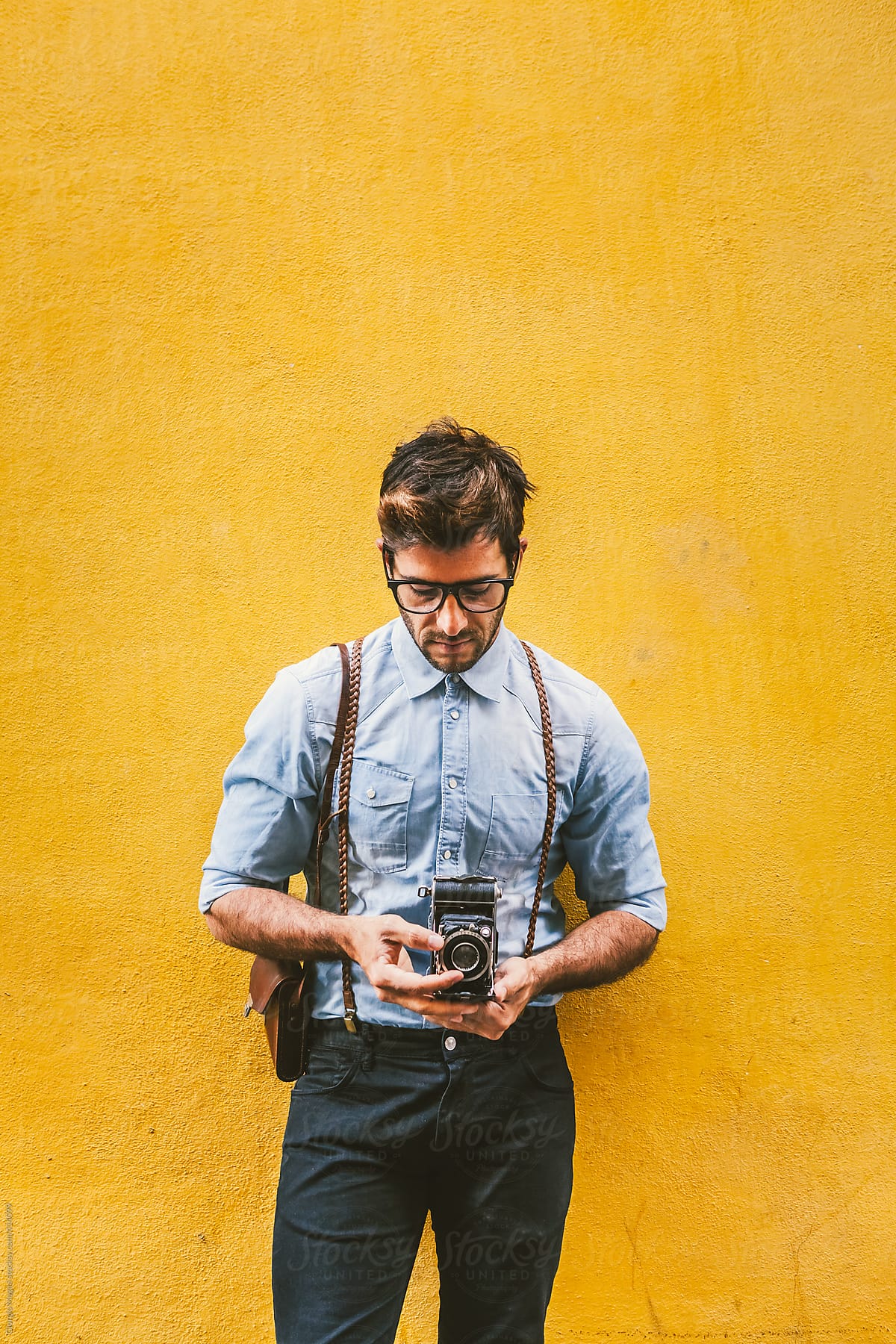 Hipster Man with Retro Camera over a Yellow Plaster Wall