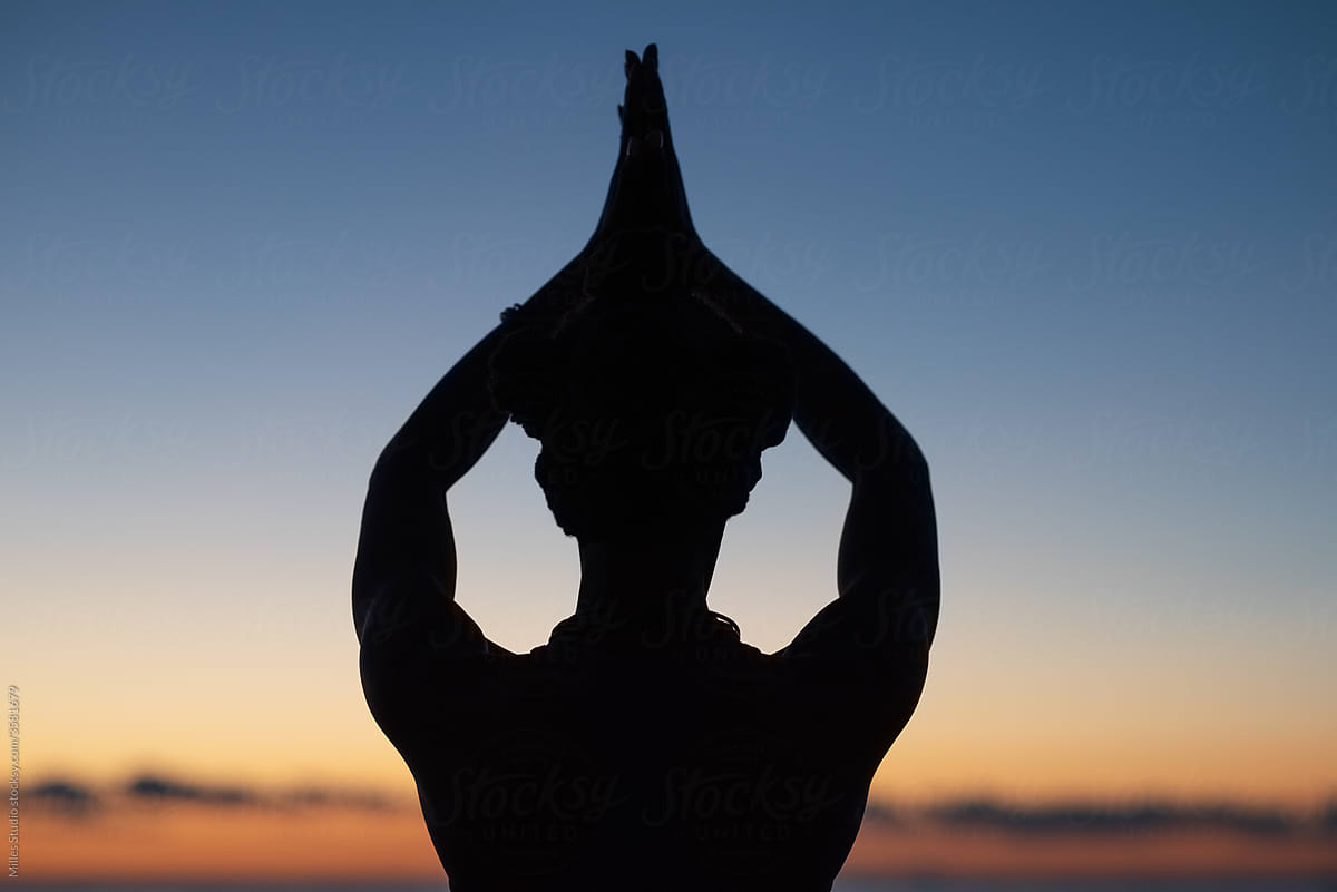 Unrecognizable female meditating with raised arms at sundown