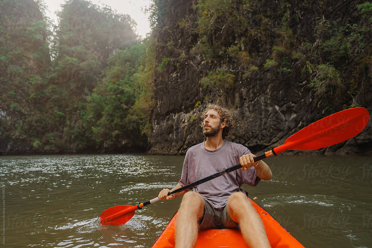 Man kayaking among islands covered in jungles at sunset