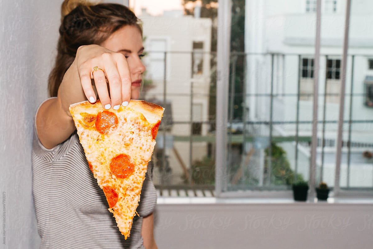 young female holding slice of pizza in front of face