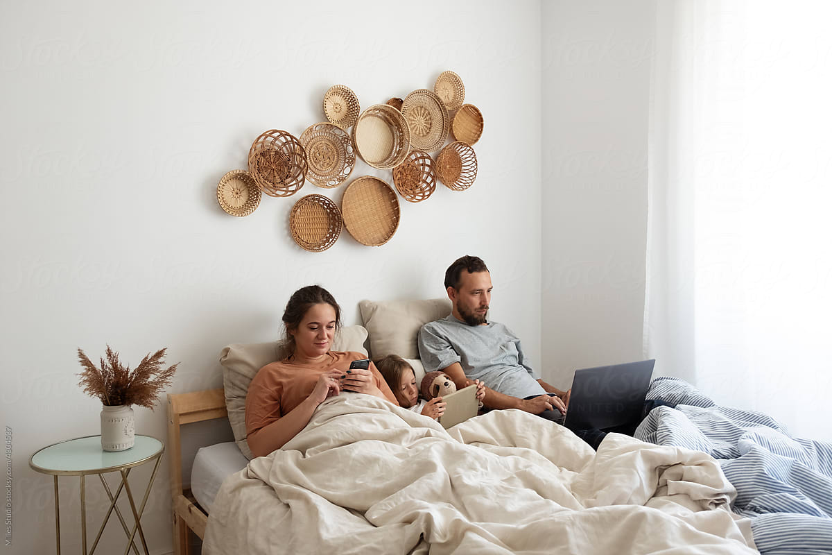 Family with gadgets chilling on bed