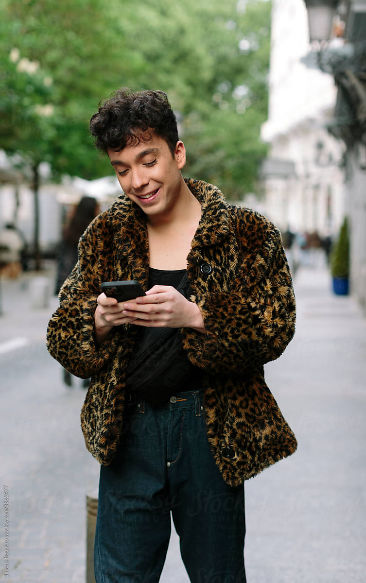 Portrait of young attractive gay man walking in the streets texting on is smartphone