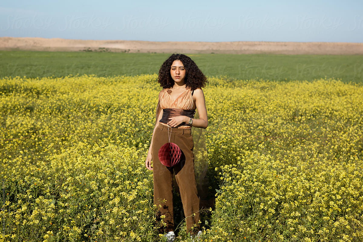Young girl with curly hair posing in a flowers field holding accessory