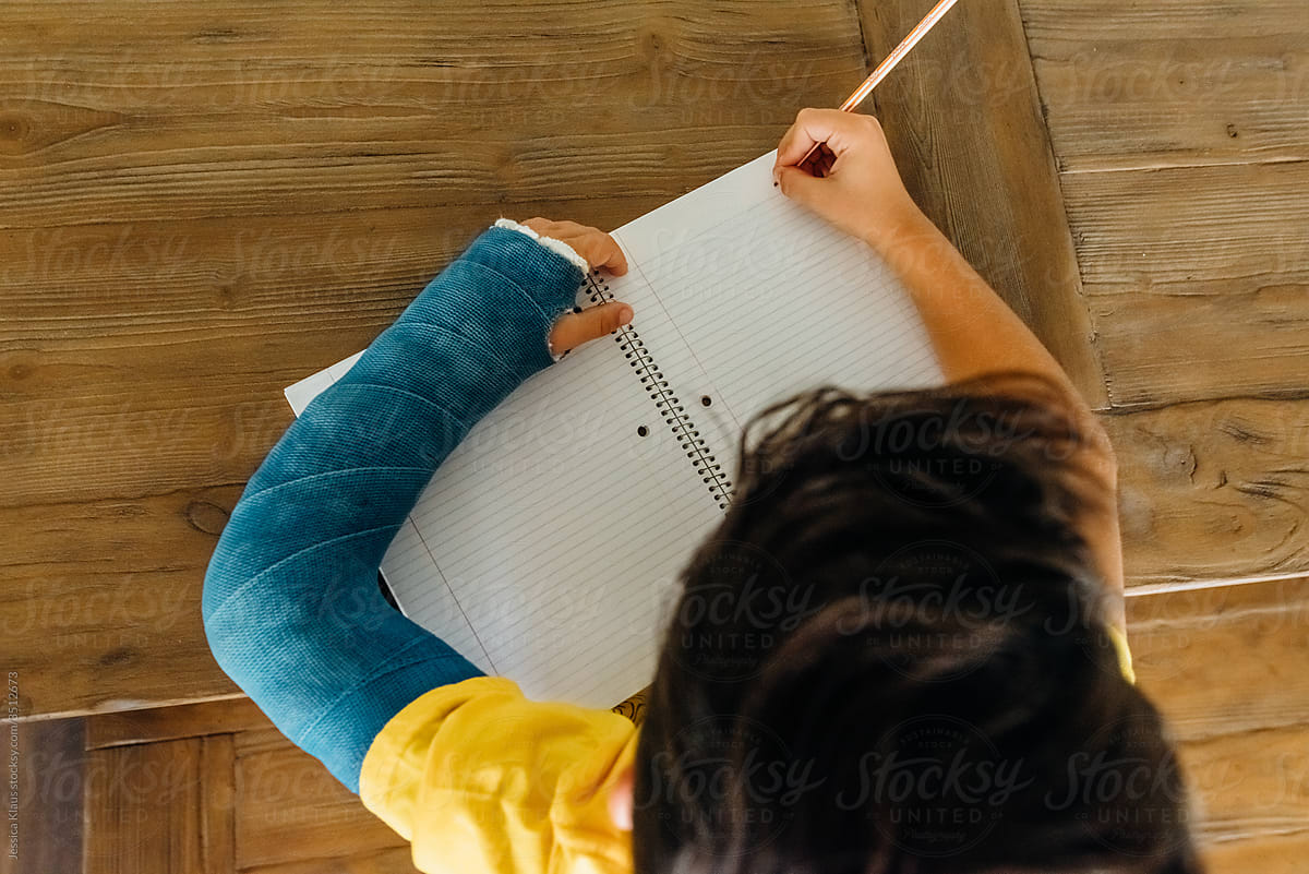Boy with a blue cast doing schoolwork.