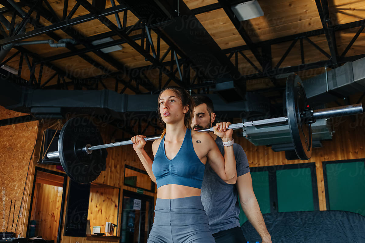 Man Helping Woman in Gym with Weightlifting