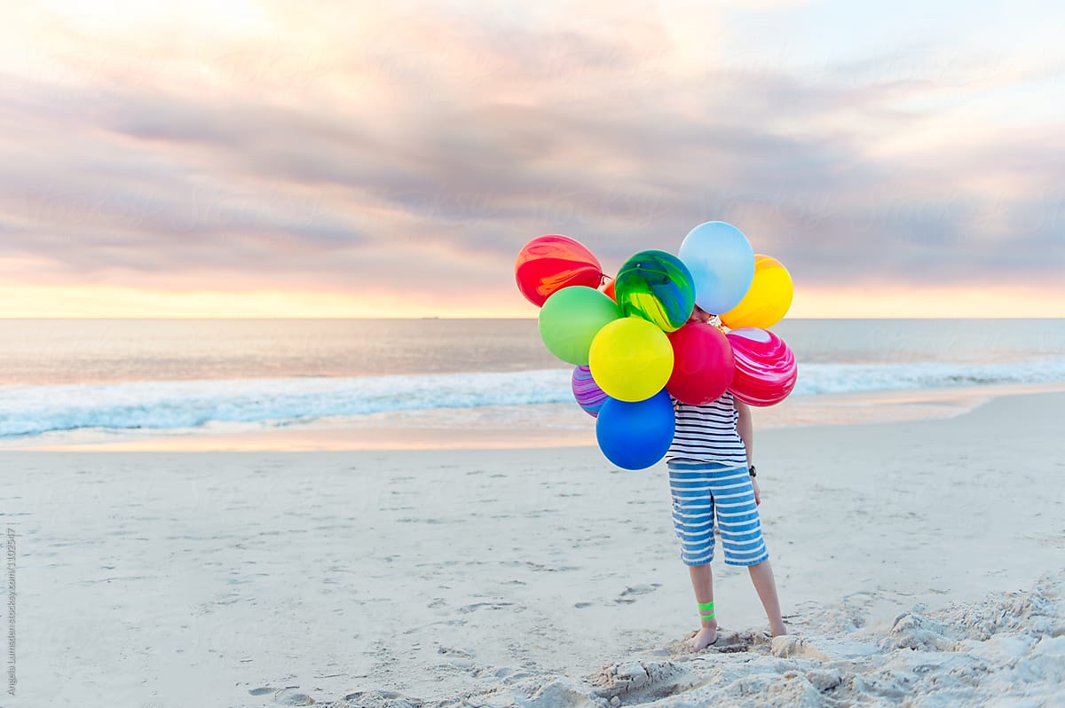 Boy standing at the beach with a large bunch of balloons