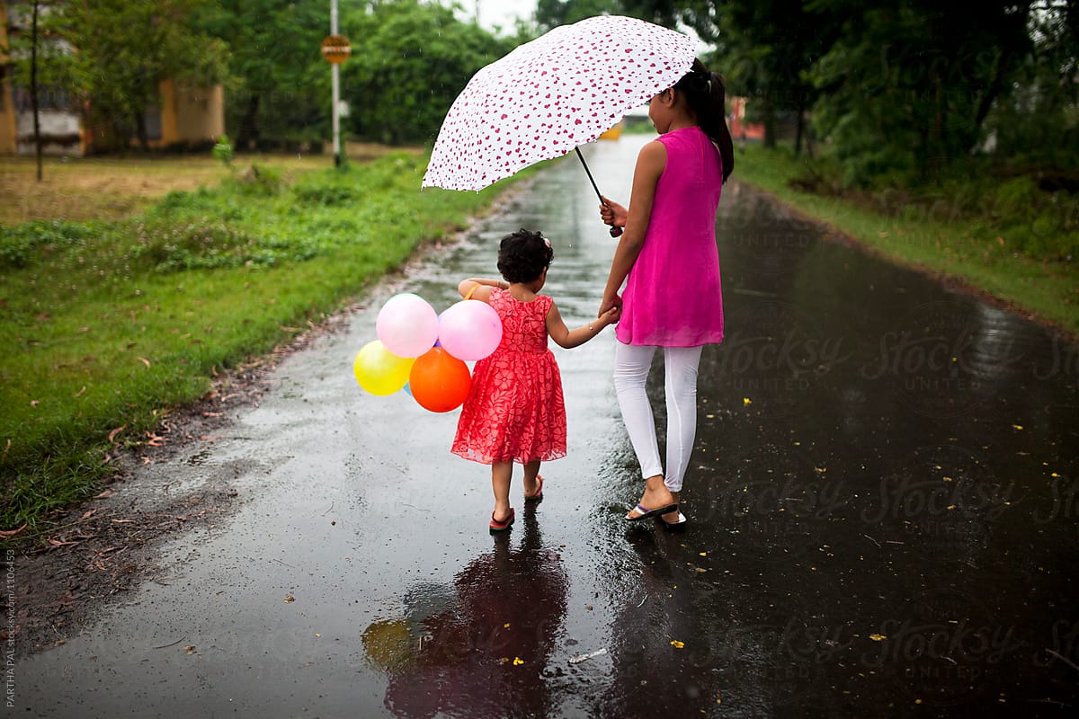 A girl and sister walking together under umbrella