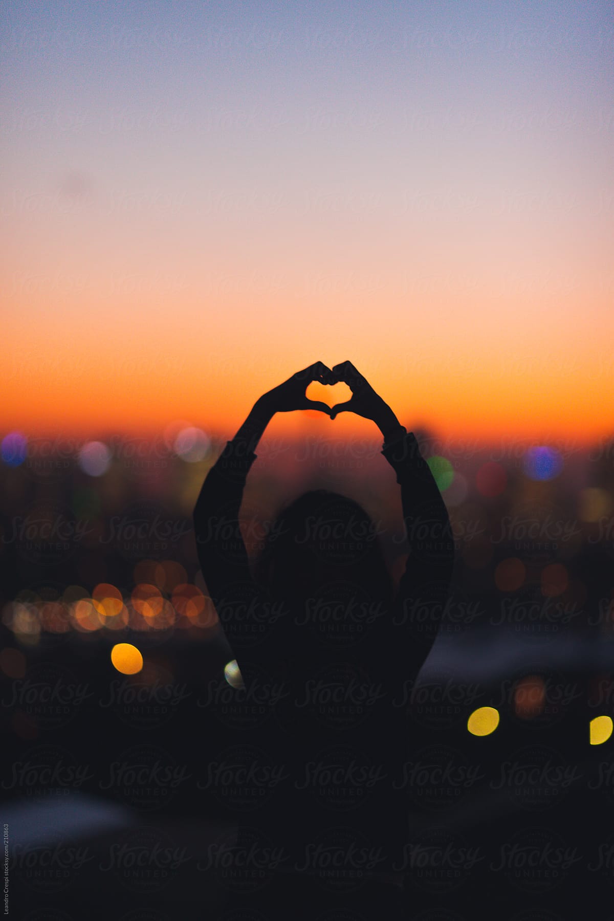 Woman in silhouette making heart shape with hands on sunset