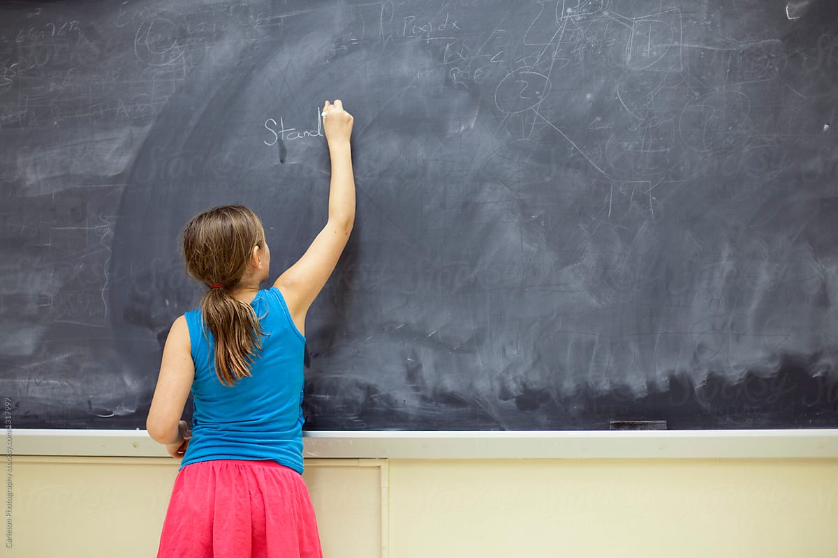 Preteen girl writes in chalk on the blackboard in front of the class