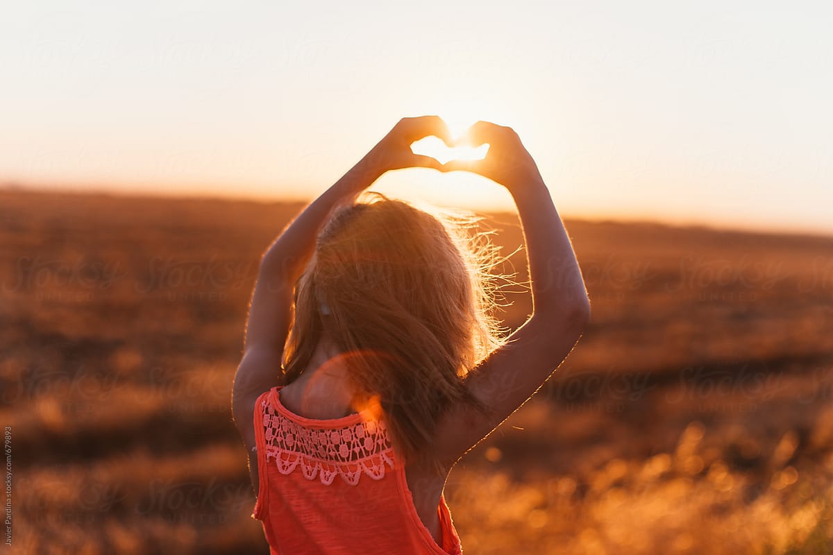 blonde girl walking at sunset doing heart with hand