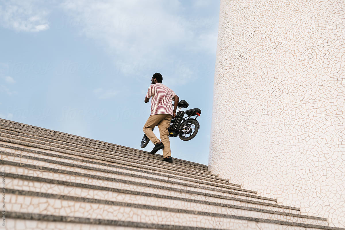 Black man carrying electric bike up stairs