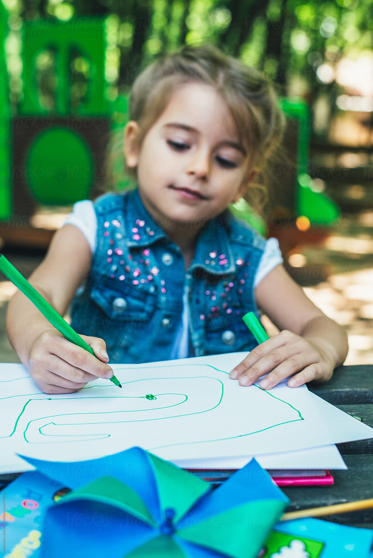 Little Blond Girl Sitting And Drawing On A Piece Of Paper Outdoors