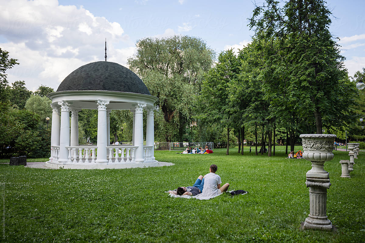 Anonymous couple seat in a park next to a round greek architecture