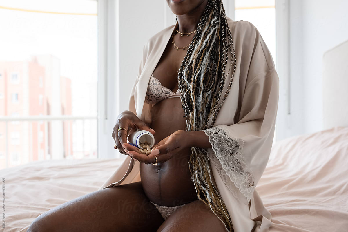 Crop black pregnant woman taking pills