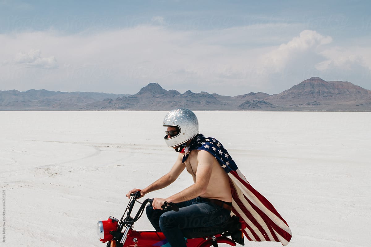 portrait of young male wearing american flag while riding motorcycle through desert salt flat