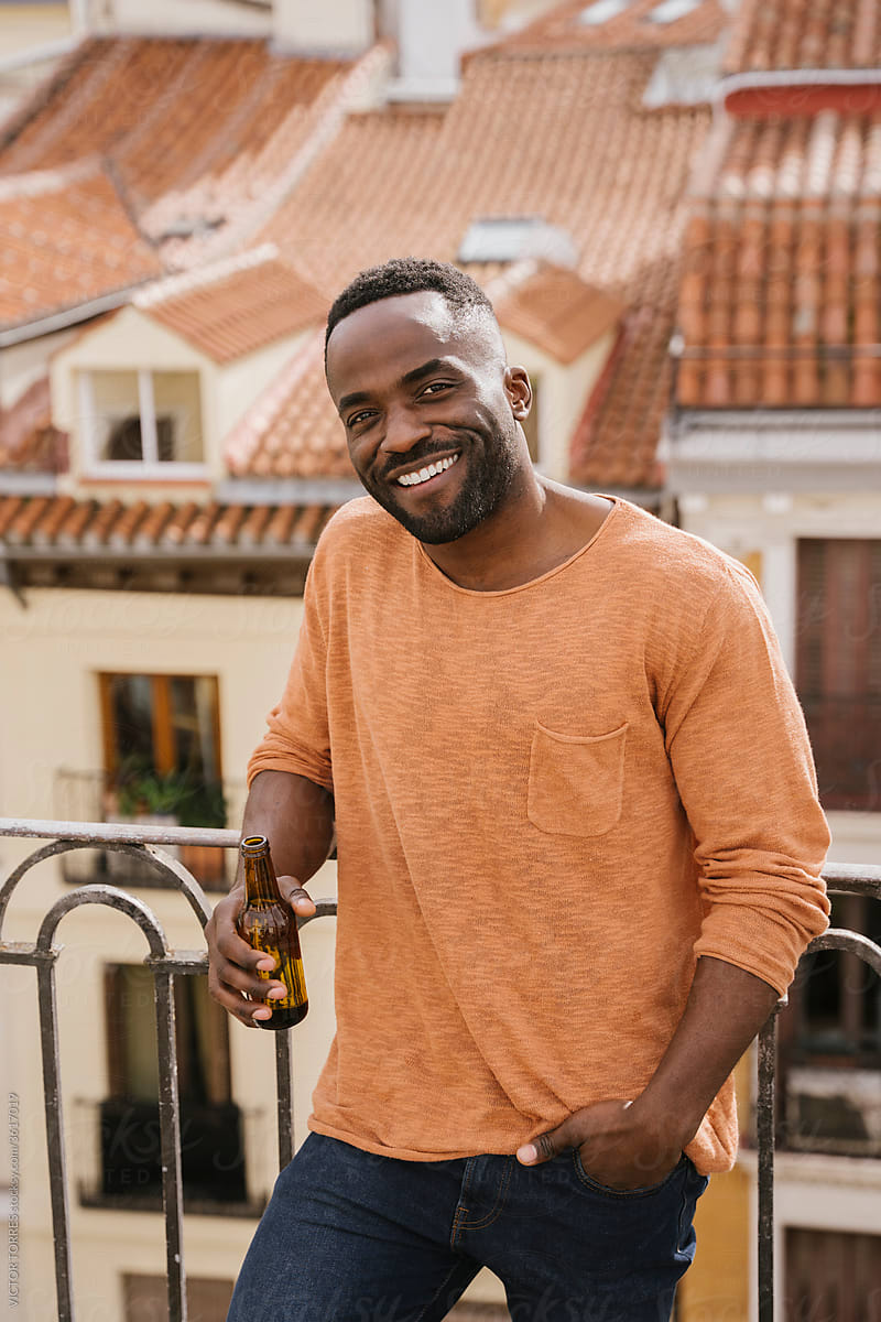 Handsome black man relaxing on balcony with bottle of beer