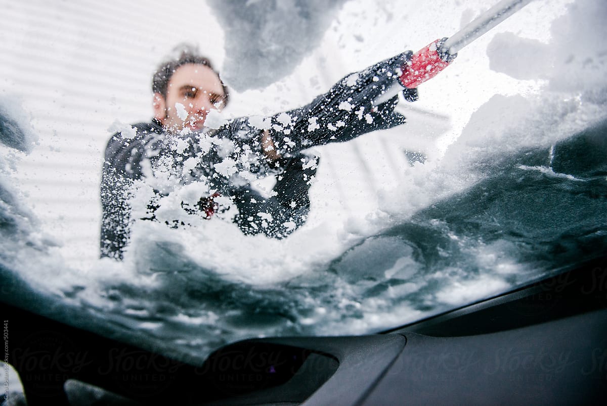 Man removes snow from the windshield of his car