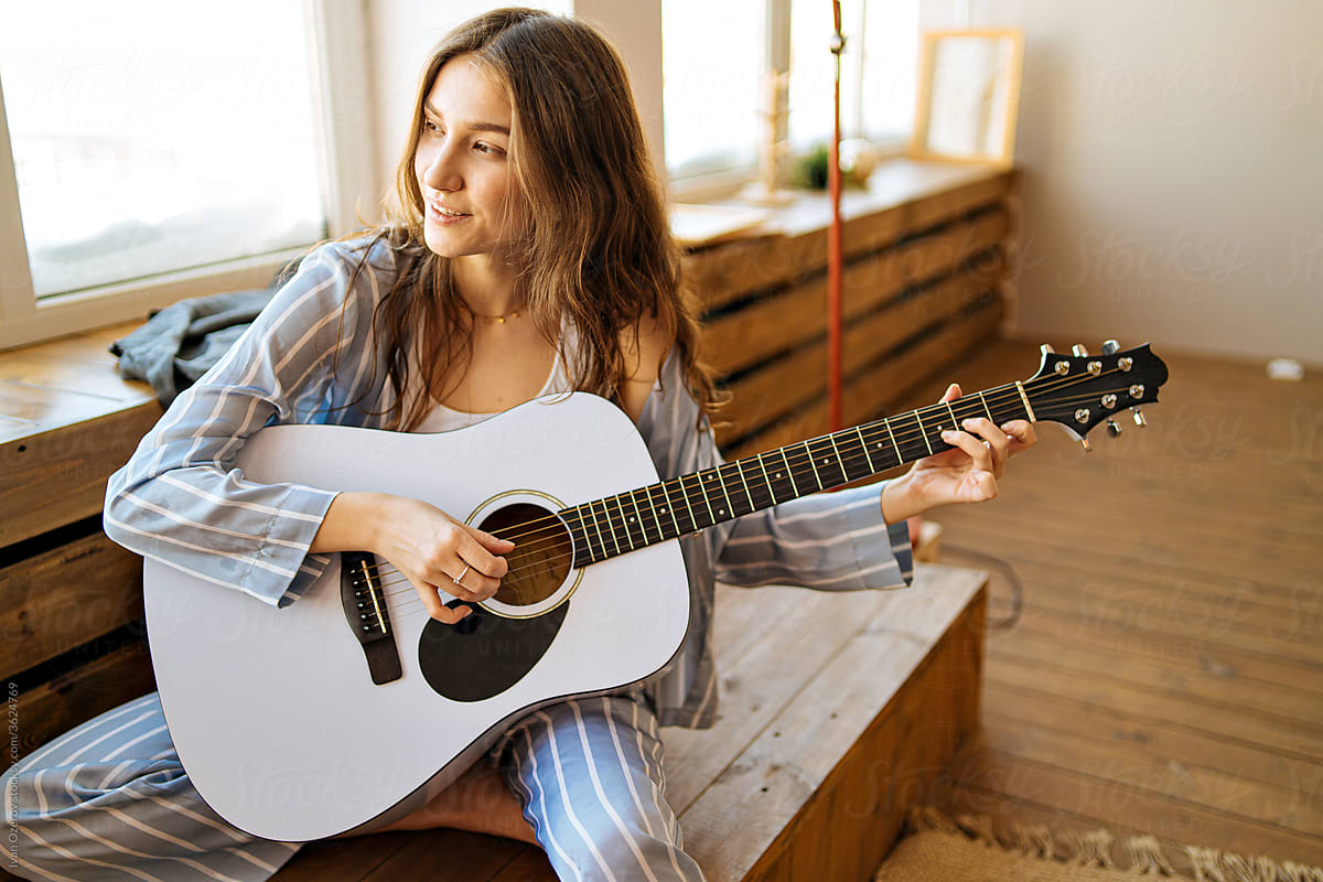 attractive young woman playing guitar at home