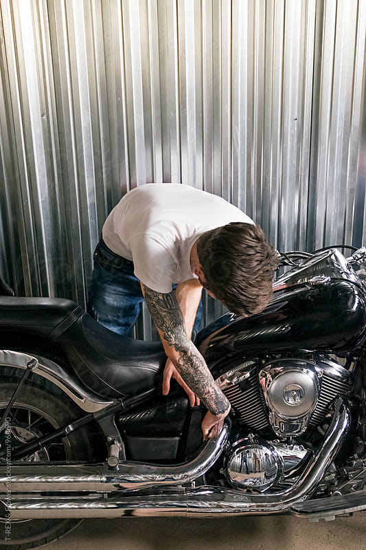 Tattooed man repairing motorbike against of metal wall