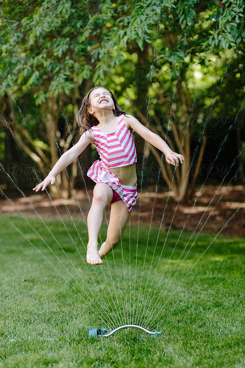 Young Girl Jumping Through A Water Sprinkler By Jakob Lagerstedt
