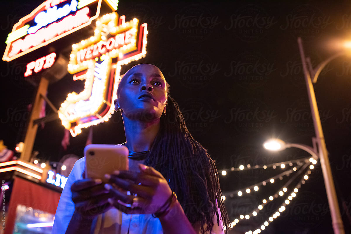 Black woman using smartphone outside pub at night