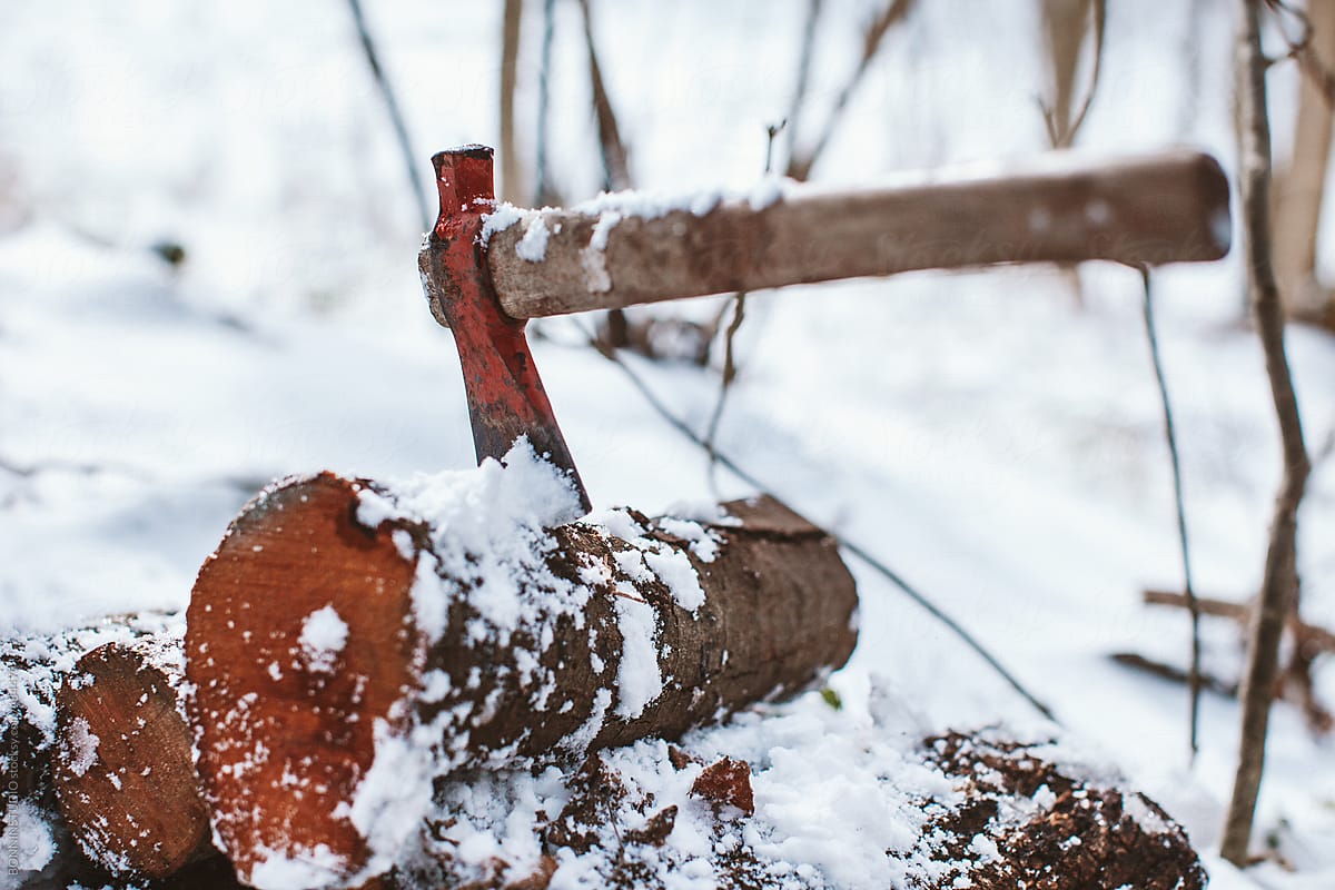Axe stack in stacked tree trunks in a snowy forest.