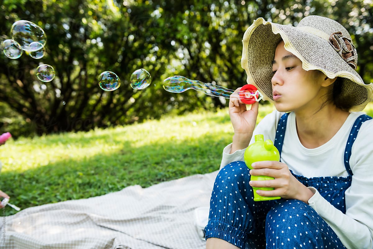 Woman sitting on picnic cloth and blowing bubbles on green grass