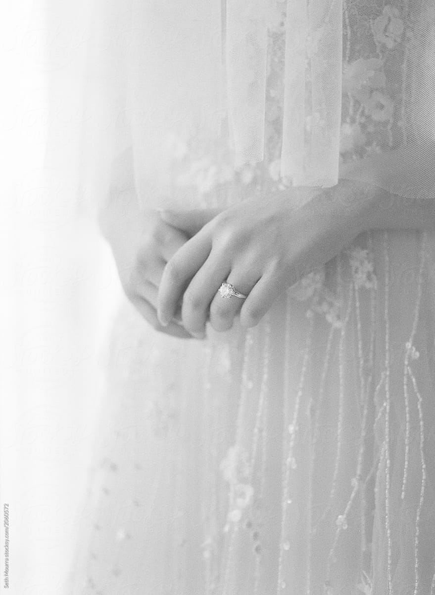 A black and white photo of a bride indoors gently holds her hands