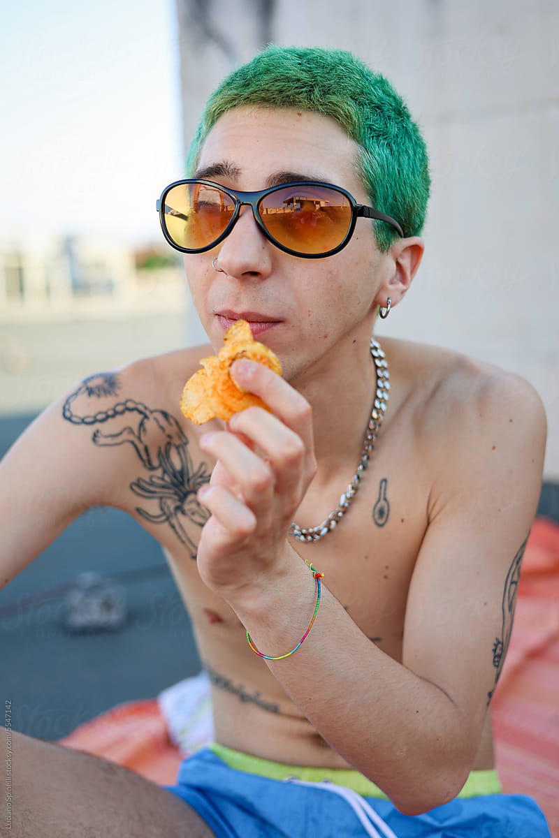 Casual Gen-Z man with colorful hair and sunglasses eating chips