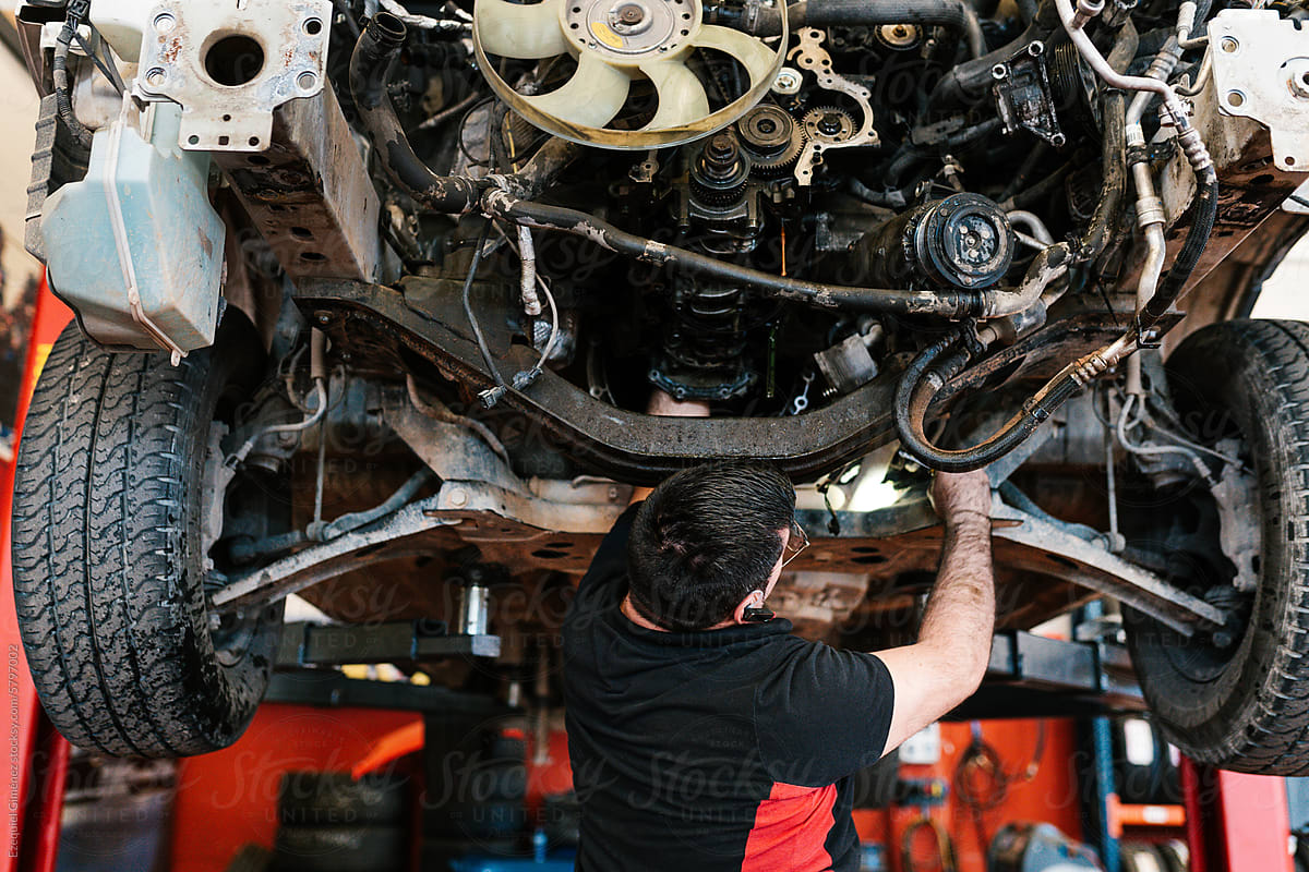 Unrecognizable mechanic repairing car engine in workshop