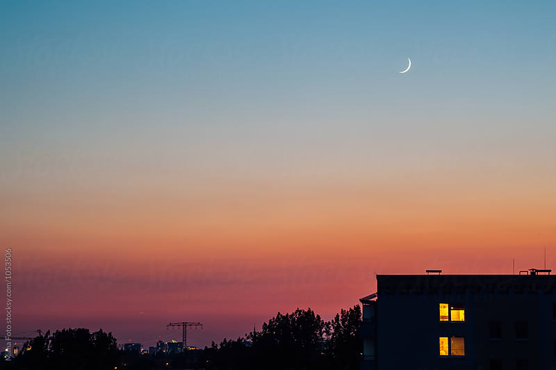 New moon over silhouetted building with lights