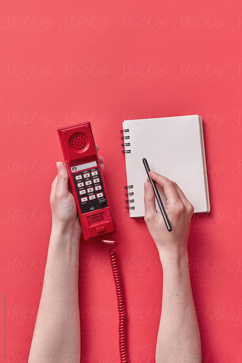 Woman holding telephone handset and writing in notebook