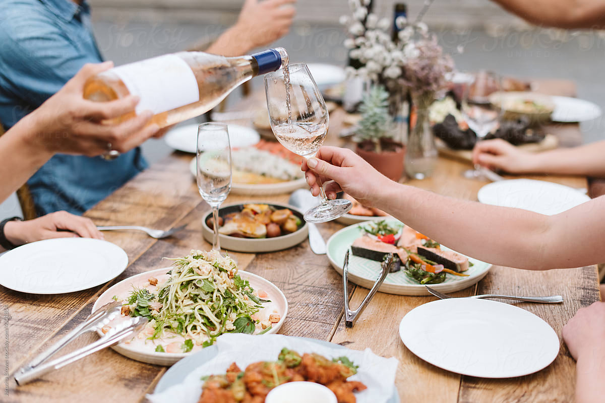 Person pours wine above a table set with colourful food.