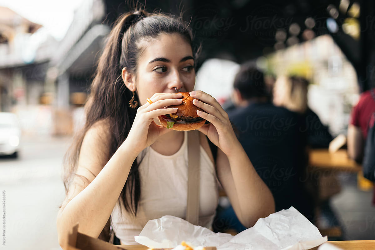 Young woman eating a hamburger with fries outdoors