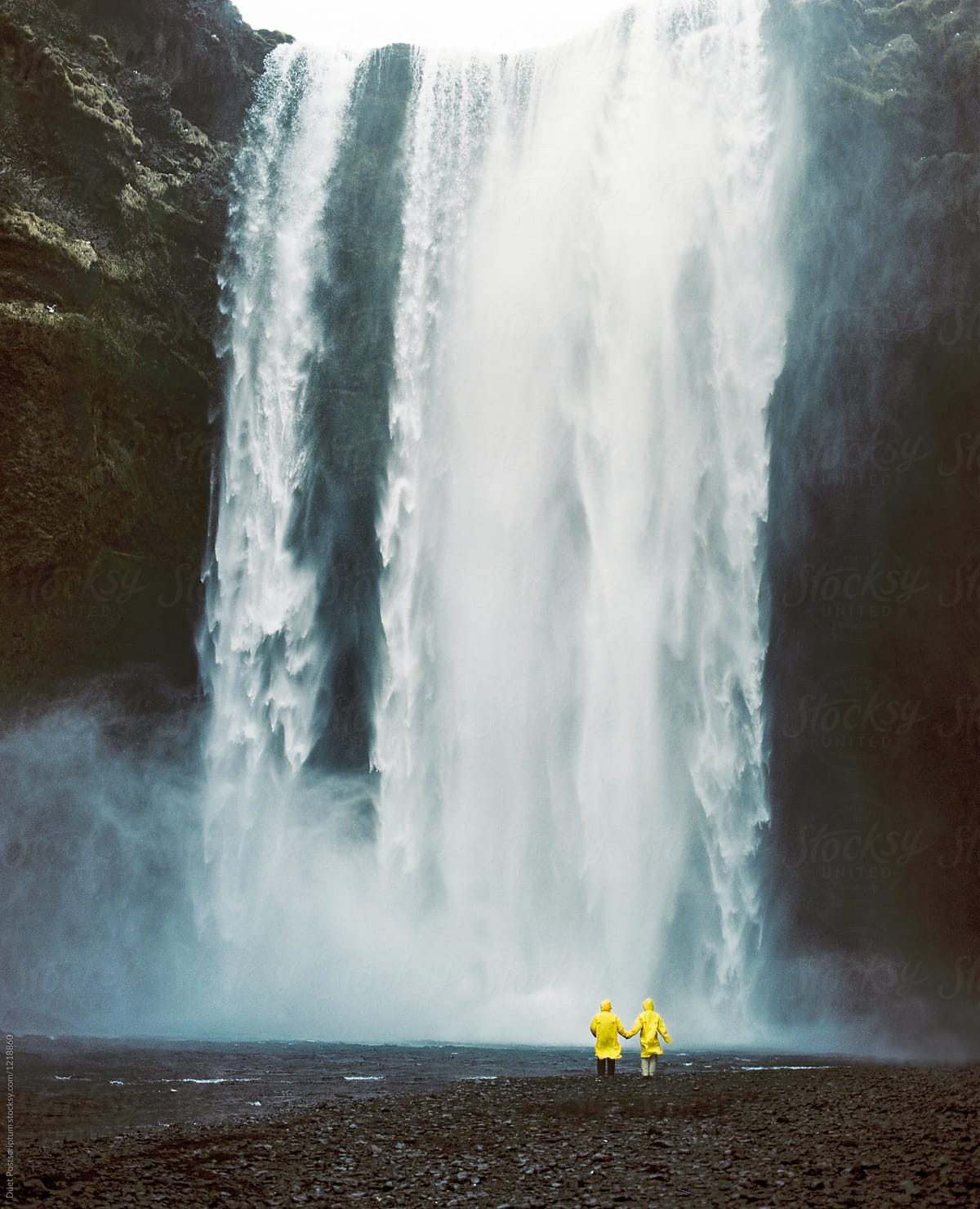 Couple in yellow raincoats on waterfall