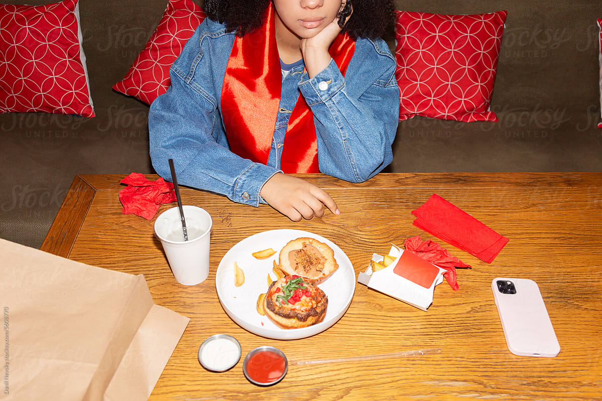 Crop black graduate sitting at table with junk food