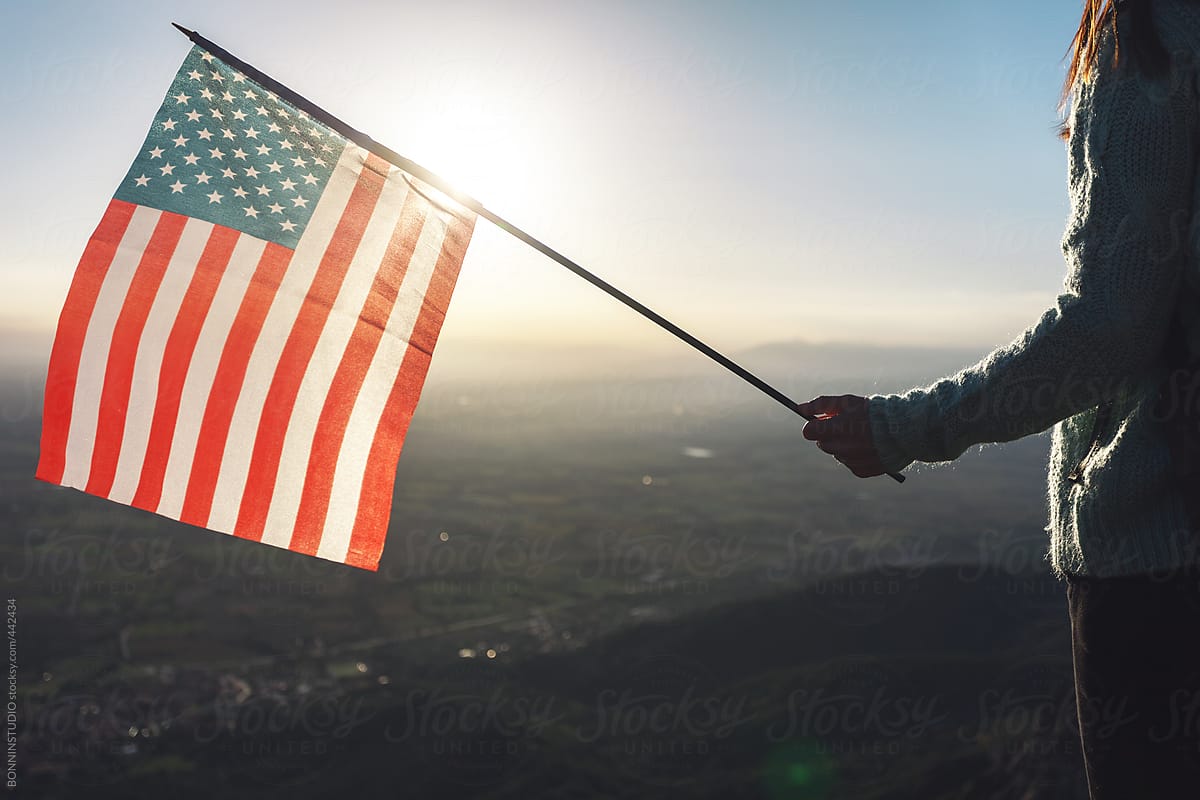 Back view of hiker woman holding an American flag on mountain peak.