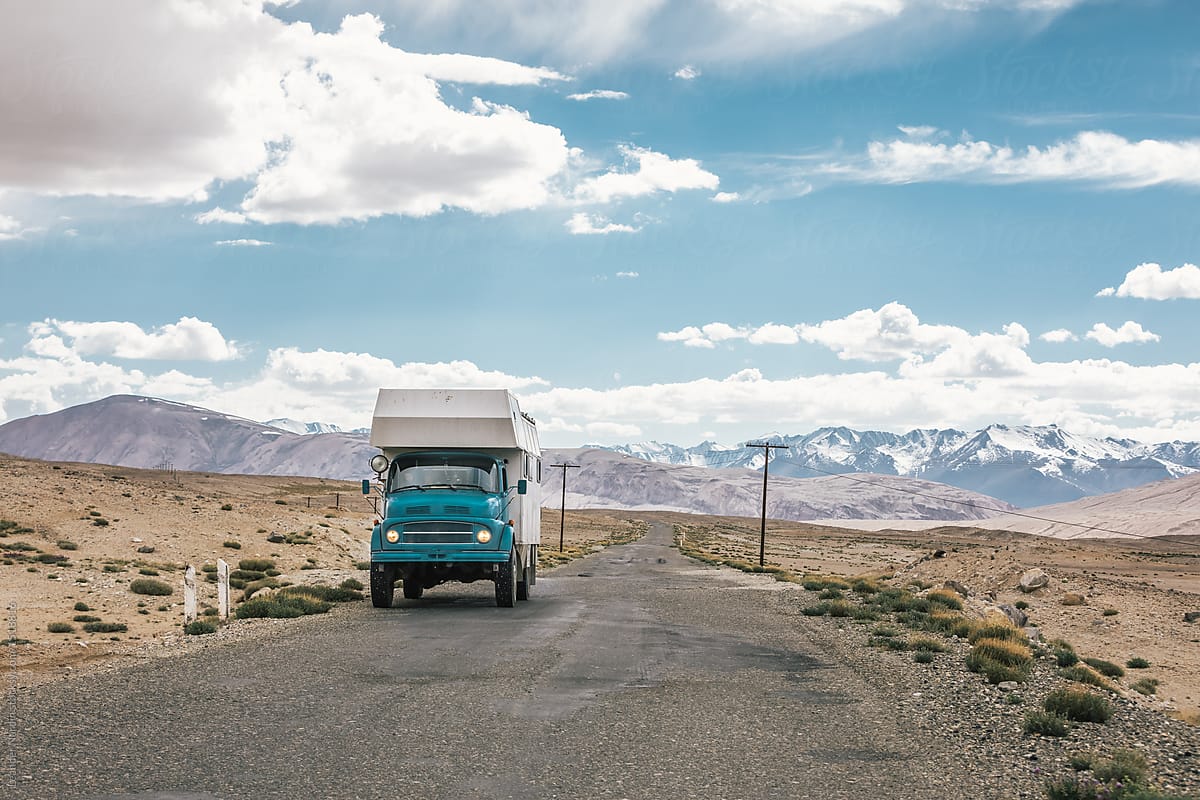 blue camping truck on bad roads on the pamir highway with snowcovered mountains in the back
