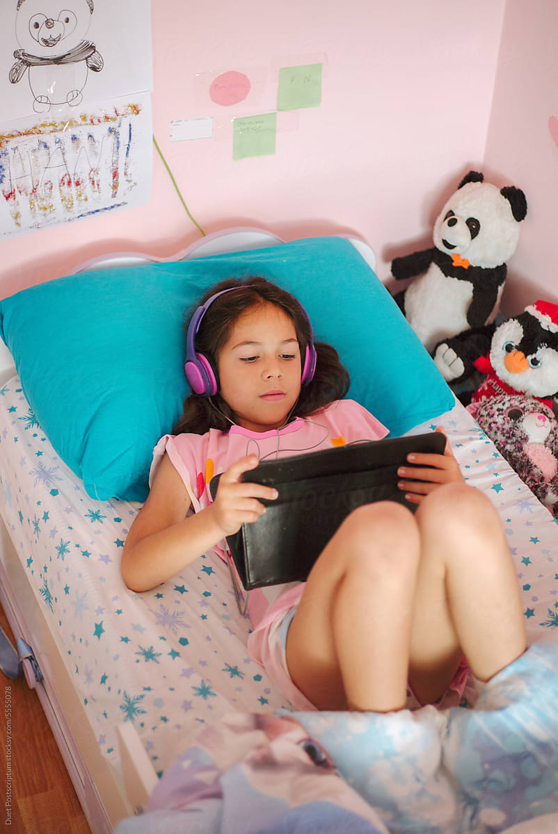 A girl watches a cartoon on a tablet lying in bed