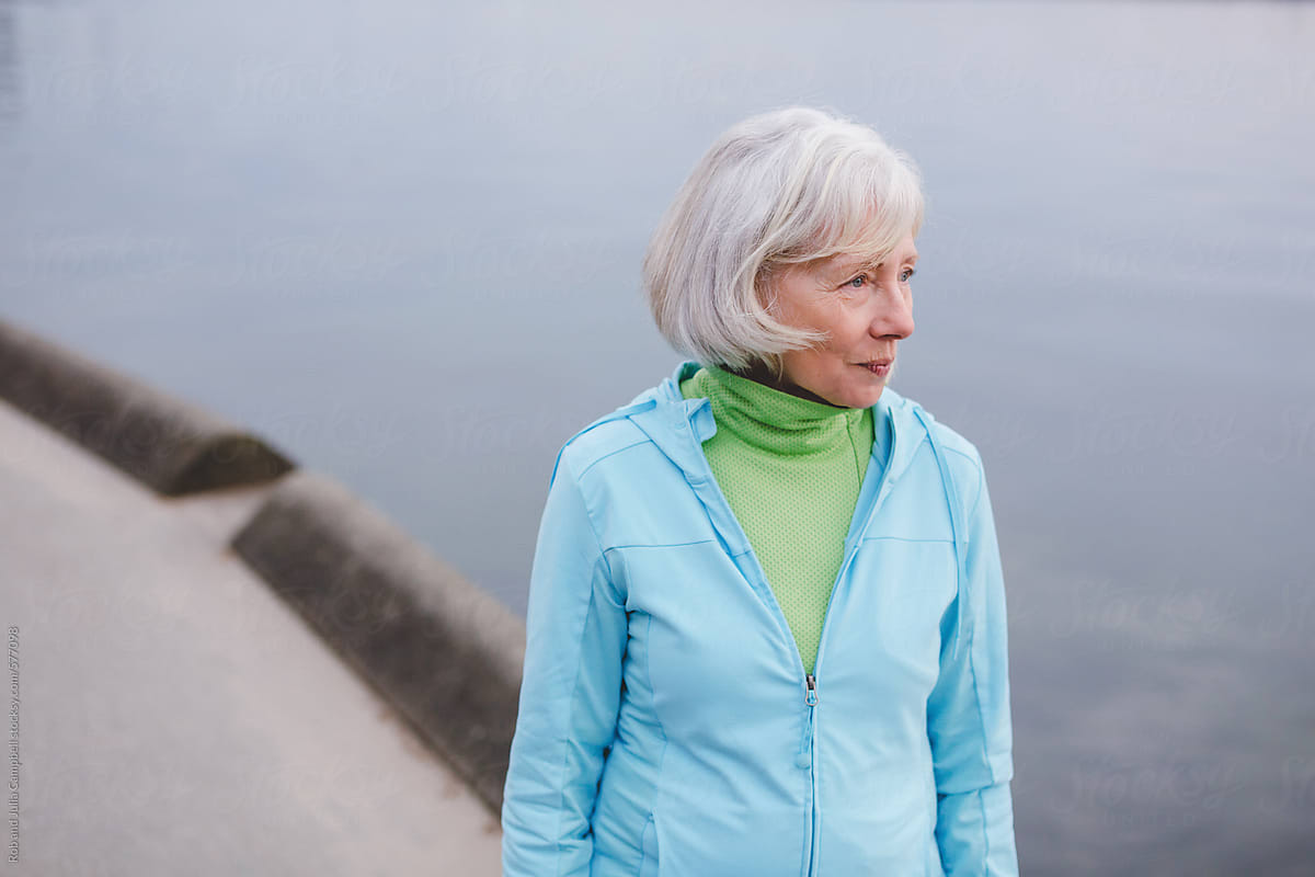 Healthy senior woman standing outside in active wear - looking at ocean