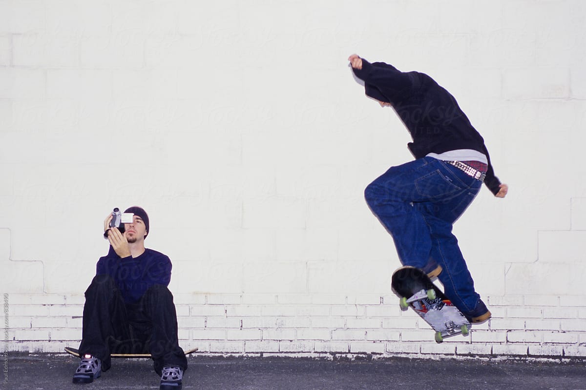 Young man making video of friend skateboarding on urban street