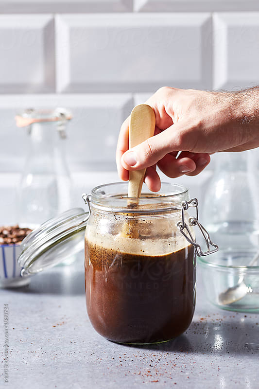 Close-up of hand stirring brew coffee in glass container