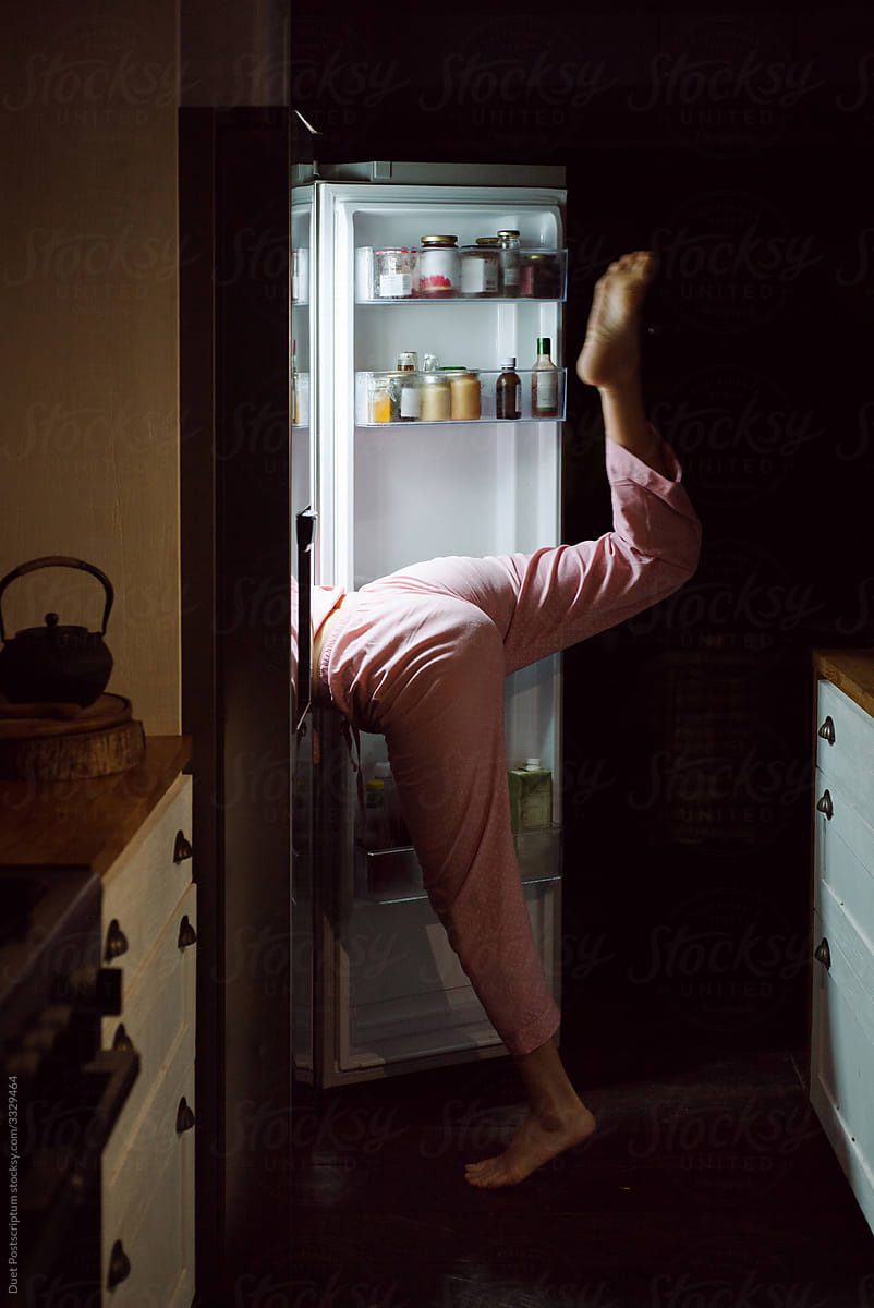 Girl in pajamas looks into the refrigerator in the kitchen at night