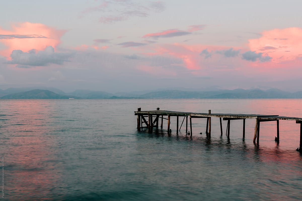 A small fishing pier in a calm sea at dawn. Pink light reflected in the sea and clouds