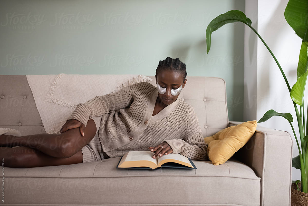 Focused black woman reading novel in apartment