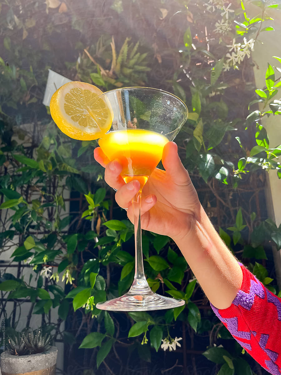 A woman\'s hand holding a yellow cocktail glass with a lime
