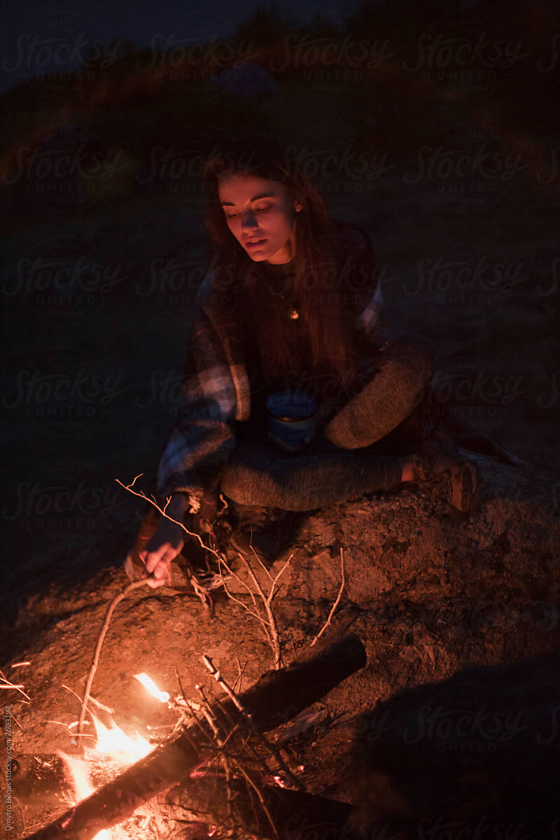 the girl in the plaid is sitting by the fire and basking