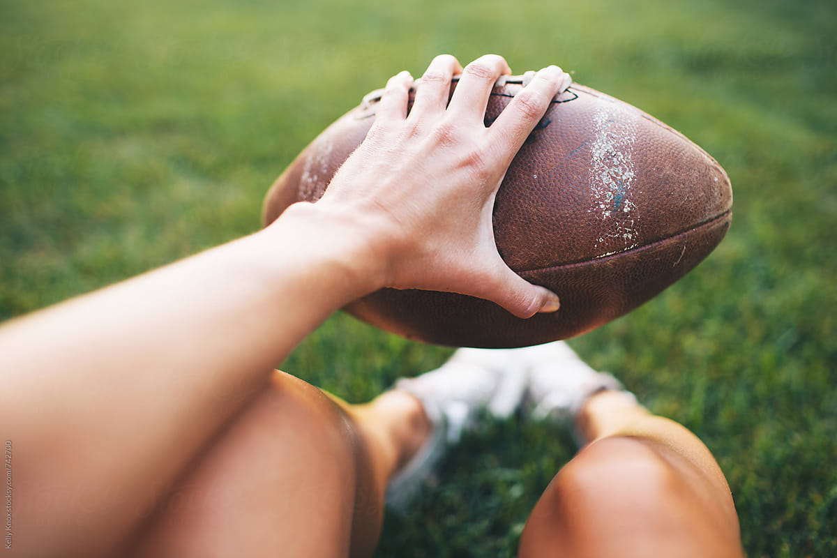 woman\'s hand holding a football in the backyard